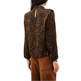 A woman shown from the back wearing a long-sleeve blouse with a black base and dense orange-brown abstract print, paired with brown pants, against a plain white background.